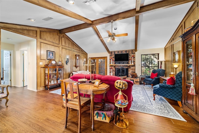 dining room featuring lofted ceiling with beams, wood walls, a brick fireplace, ceiling fan, and light hardwood / wood-style flooring