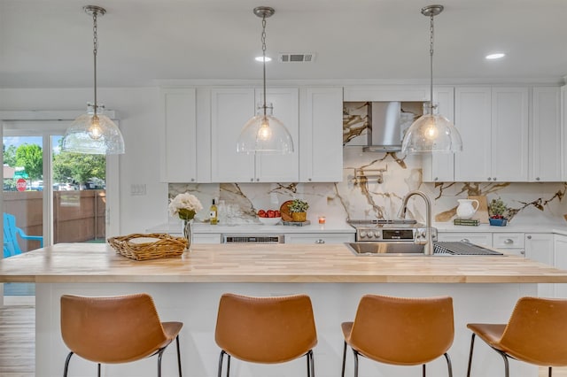 kitchen with a center island with sink, hanging light fixtures, ventilation hood, a breakfast bar, and white cabinetry