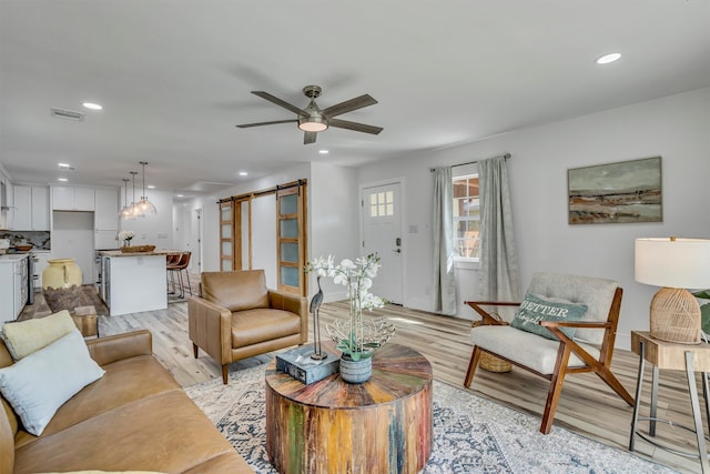 living room with light wood-type flooring, a barn door, and ceiling fan