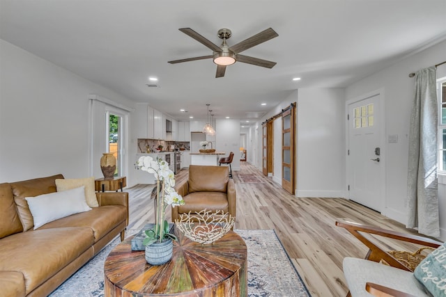 living room featuring a barn door, ceiling fan, and light wood-type flooring