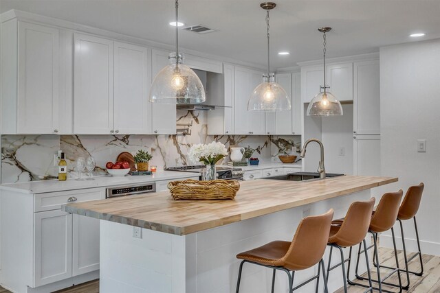 kitchen featuring wooden counters, white cabinetry, sink, and an island with sink