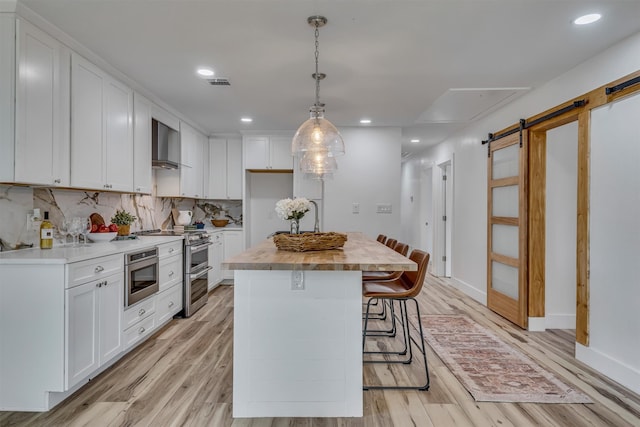 kitchen featuring stainless steel appliances, white cabinetry, a center island, a barn door, and light wood-type flooring