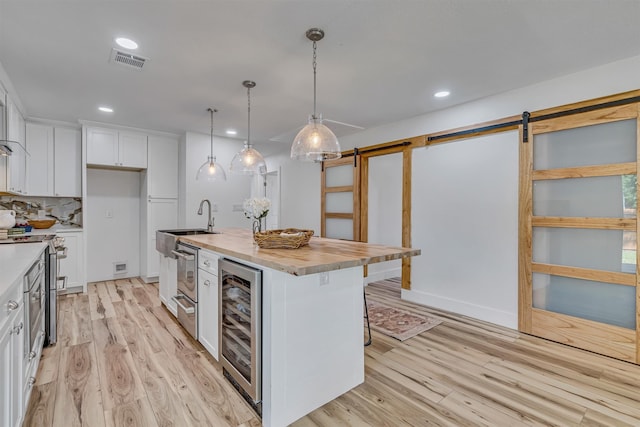 kitchen with beverage cooler, white cabinets, hanging light fixtures, a barn door, and an island with sink