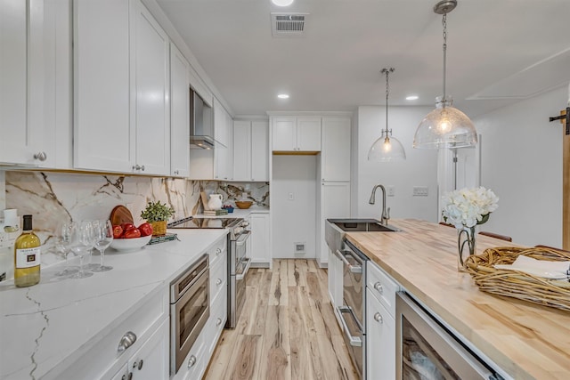 kitchen with butcher block counters, hanging light fixtures, sink, white cabinets, and light hardwood / wood-style flooring