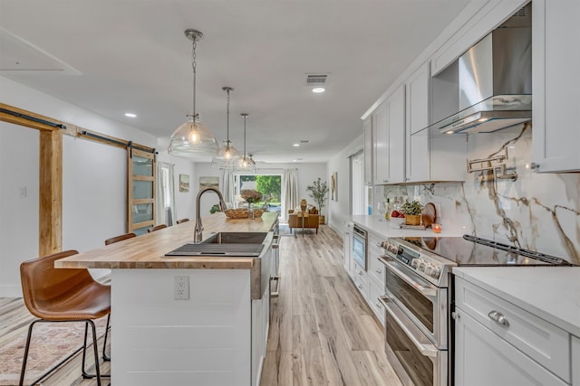 kitchen with a barn door, white cabinetry, an island with sink, and appliances with stainless steel finishes