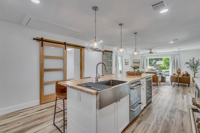 kitchen with white cabinetry, a barn door, hanging light fixtures, light hardwood / wood-style floors, and a kitchen island with sink