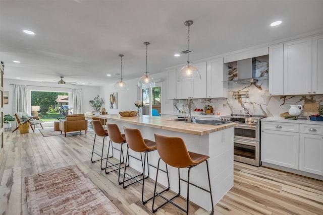 kitchen featuring white cabinets, light wood-type flooring, double oven range, and wall chimney range hood