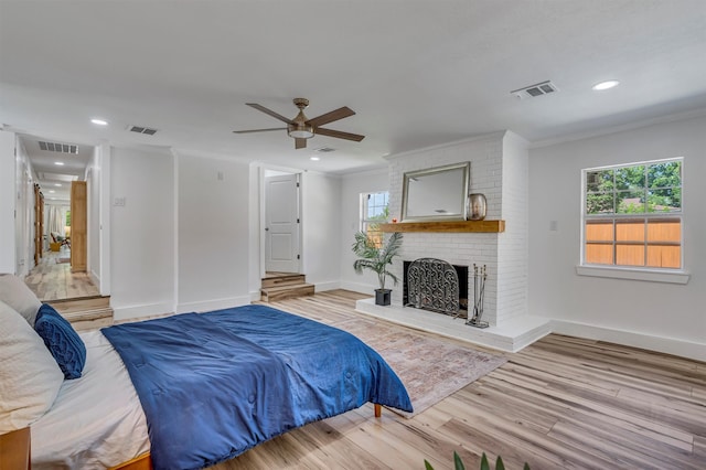 bedroom with a brick fireplace, light hardwood / wood-style floors, ceiling fan, and crown molding