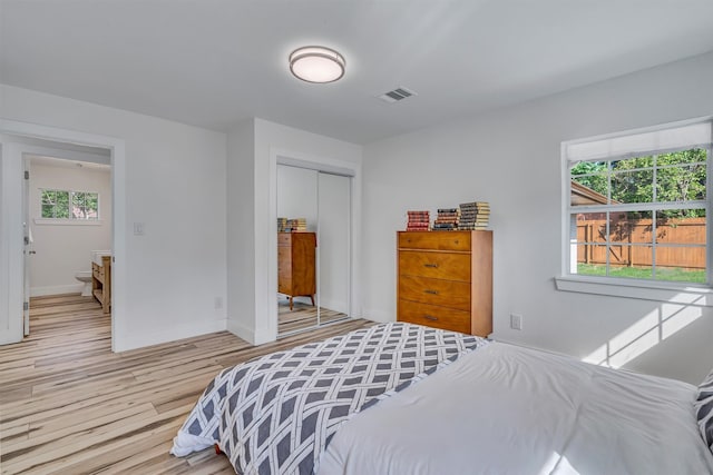 bedroom featuring ensuite bathroom, hardwood / wood-style floors, multiple windows, and a closet