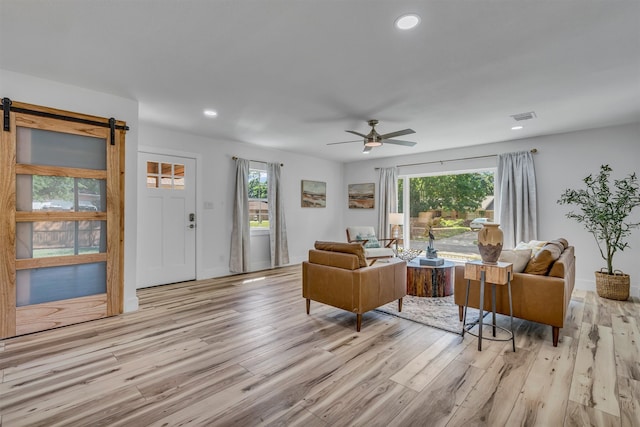 living room with light hardwood / wood-style flooring, a barn door, ceiling fan, and plenty of natural light