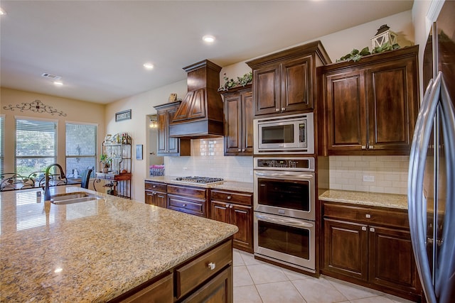 kitchen with premium range hood, sink, appliances with stainless steel finishes, and light stone counters