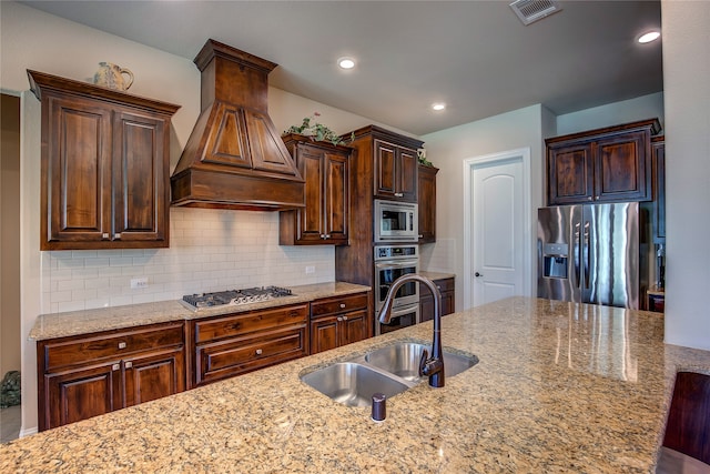 kitchen featuring custom range hood, sink, decorative backsplash, stainless steel appliances, and light stone counters