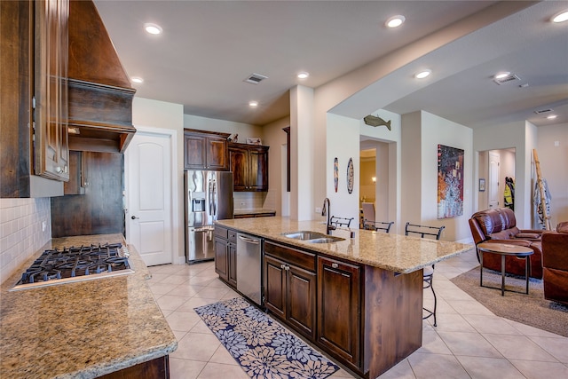 kitchen featuring decorative backsplash, a breakfast bar, stainless steel appliances, a kitchen island with sink, and sink