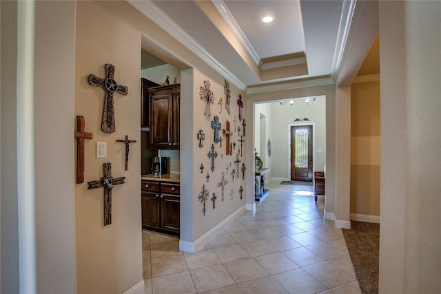 corridor with ornamental molding, light tile patterned floors, and a tray ceiling