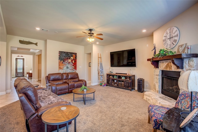 living room featuring light carpet, a stone fireplace, and ceiling fan