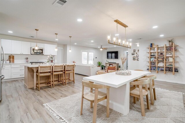 dining room with ceiling fan with notable chandelier and light wood-type flooring