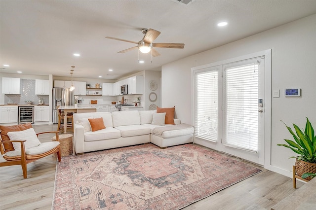 living room with ceiling fan, beverage cooler, and light wood-type flooring