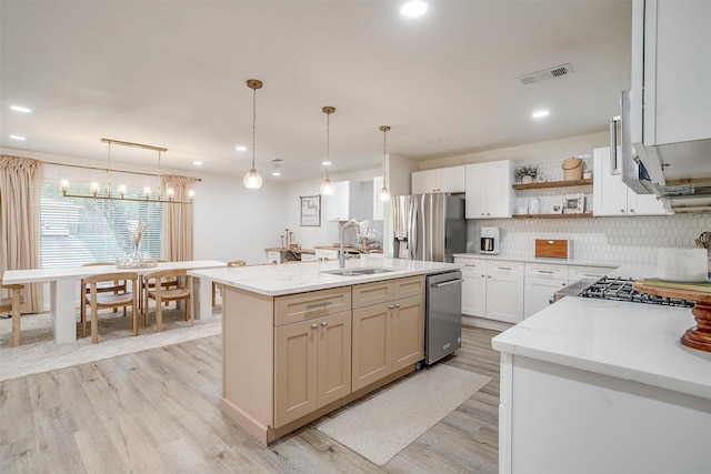 kitchen featuring light stone counters, appliances with stainless steel finishes, decorative light fixtures, and a center island with sink