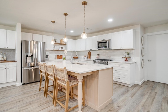 kitchen featuring appliances with stainless steel finishes, sink, white cabinets, hanging light fixtures, and a center island with sink