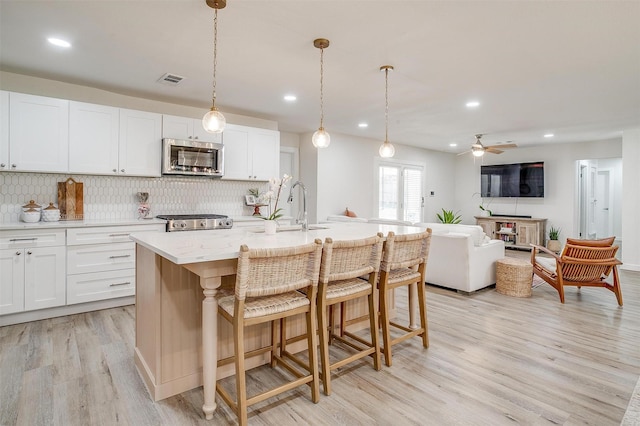 kitchen with an island with sink, sink, white cabinets, backsplash, and stove