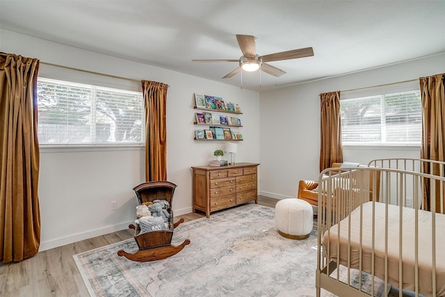 bedroom featuring light hardwood / wood-style flooring, a nursery area, and ceiling fan