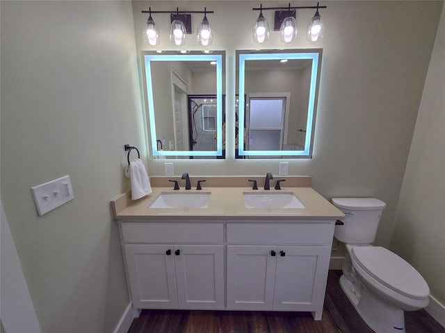 bathroom with toilet, double vanity, a sink, and wood finished floors