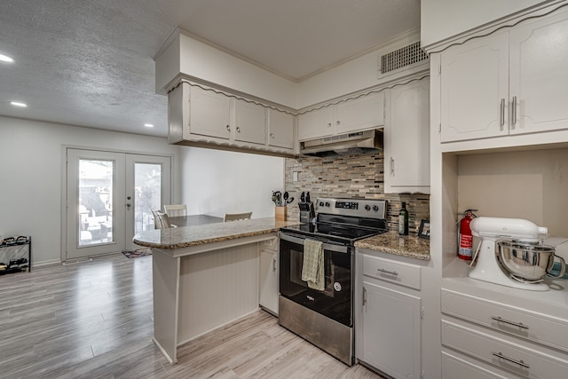 kitchen with light hardwood / wood-style floors, kitchen peninsula, a textured ceiling, stainless steel range with electric stovetop, and french doors