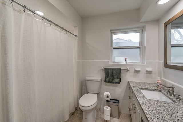 bathroom featuring a wealth of natural light, vanity, toilet, and tile walls