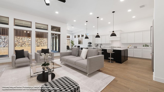 living room with ceiling fan, light hardwood / wood-style floors, sink, and a towering ceiling