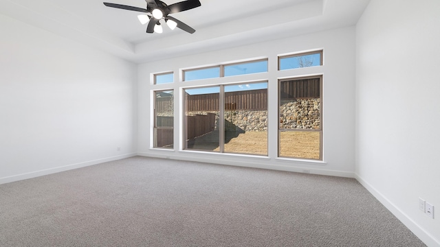 carpeted empty room with a raised ceiling and ceiling fan