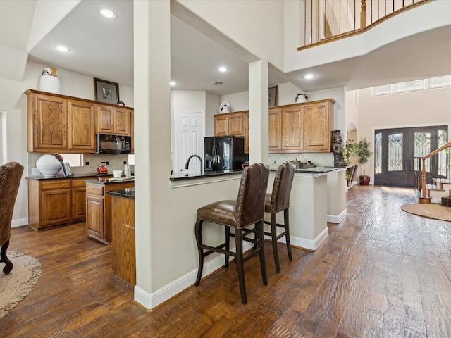 kitchen with tasteful backsplash, dark wood-type flooring, a kitchen bar, and black appliances