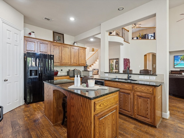 kitchen with sink, dark stone countertops, black fridge with ice dispenser, kitchen peninsula, and dark wood-type flooring