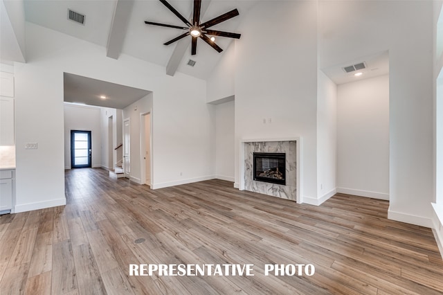 unfurnished living room featuring a tile fireplace, high vaulted ceiling, ceiling fan, beam ceiling, and light hardwood / wood-style flooring