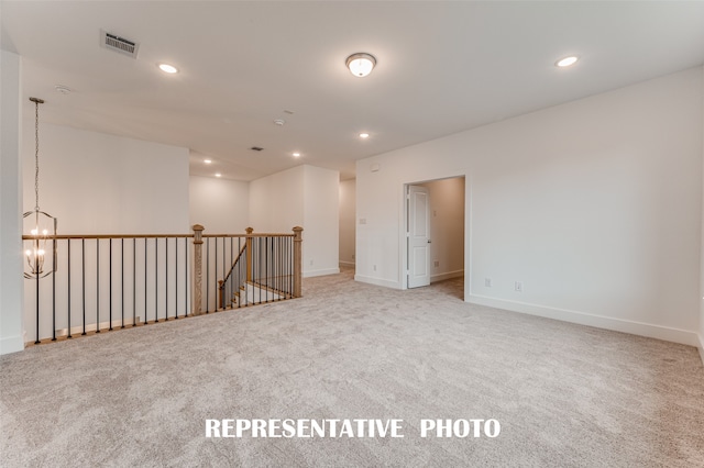 spare room featuring light carpet and a notable chandelier