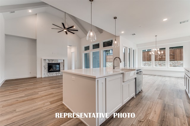 kitchen featuring a center island with sink, white cabinetry, sink, a high end fireplace, and light hardwood / wood-style flooring