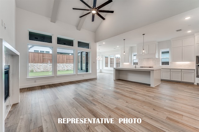 unfurnished living room with beamed ceiling, ceiling fan with notable chandelier, light wood-type flooring, and high vaulted ceiling