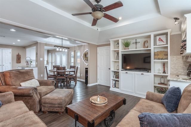 living room with dark hardwood / wood-style floors, sink, ceiling fan with notable chandelier, and a tray ceiling