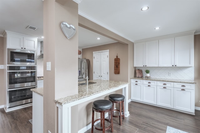 kitchen with light stone counters, crown molding, white cabinets, dark wood-type flooring, and decorative backsplash