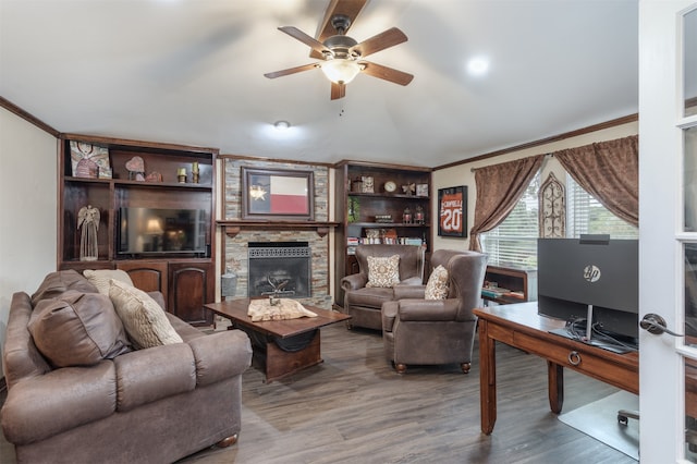 living room featuring a stone fireplace, hardwood / wood-style floors, ceiling fan, and crown molding