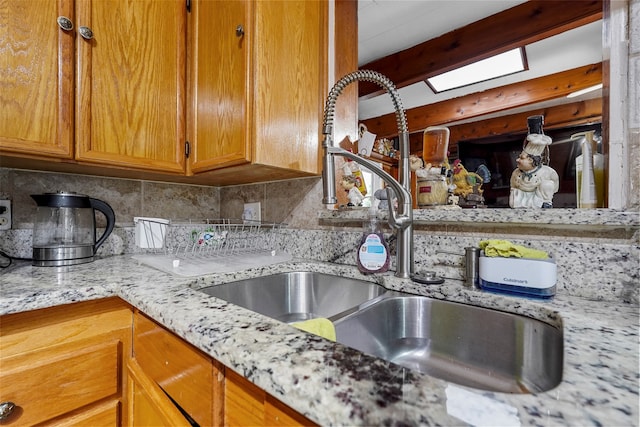 room details featuring decorative backsplash, light stone countertops, a skylight, and sink