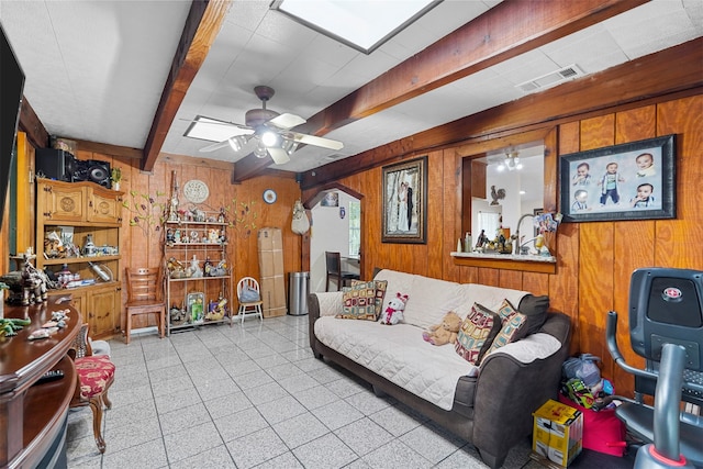 living room with wood walls, beamed ceiling, and ceiling fan