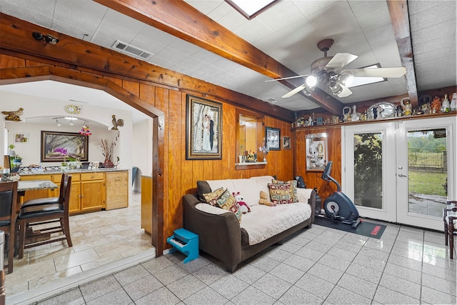 living room with french doors, beamed ceiling, wooden walls, and ceiling fan