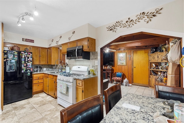 kitchen with white gas range, sink, black refrigerator with ice dispenser, light tile patterned floors, and backsplash