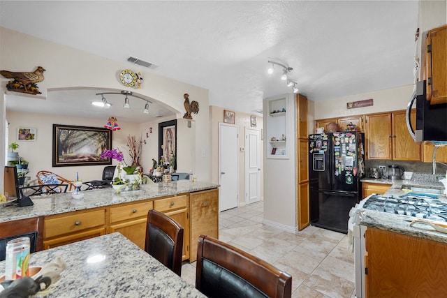 kitchen with light stone countertops, black fridge, white range with gas cooktop, and light tile patterned flooring