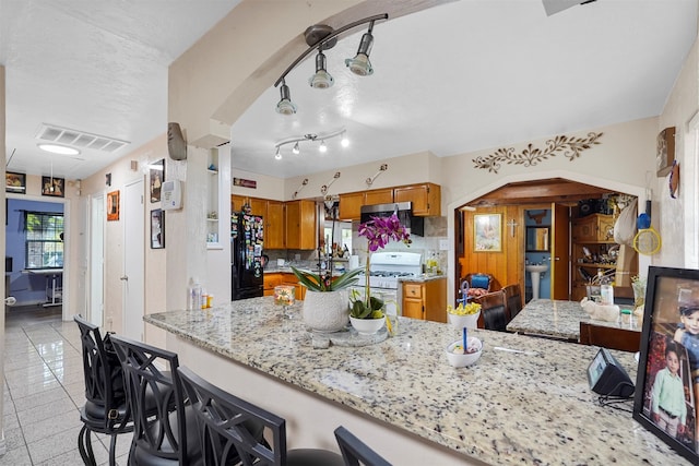 kitchen with white gas range, black fridge, light stone counters, kitchen peninsula, and a kitchen breakfast bar