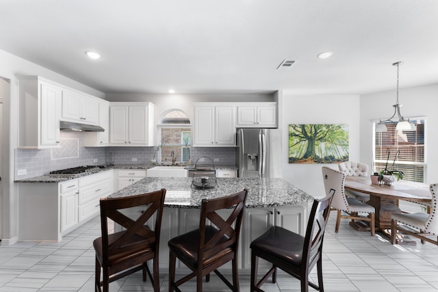 kitchen with a wealth of natural light, light stone countertops, a kitchen island, and appliances with stainless steel finishes