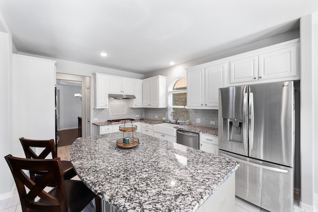 kitchen with stone counters, stainless steel appliances, a kitchen island, and white cabinetry