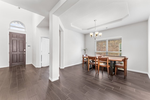 dining space featuring a tray ceiling, a wealth of natural light, dark wood-type flooring, and an inviting chandelier