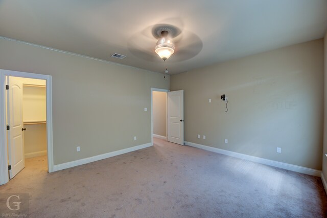 unfurnished bedroom with ceiling fan, light carpet, a closet, and a walk in closet