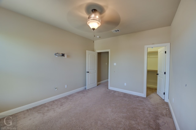 unfurnished bedroom with a closet, a walk in closet, light carpet, and ceiling fan